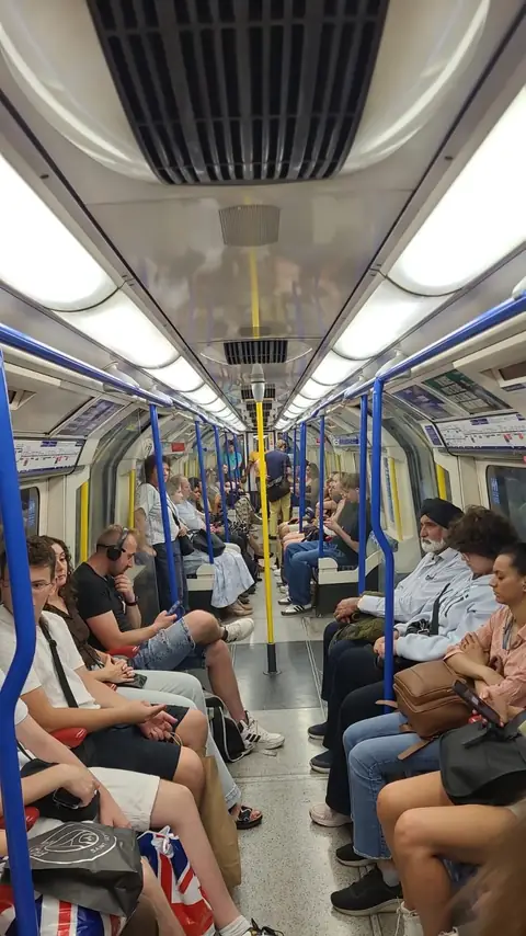 Londra metrosunun vagonunda oturan yolcular ve öğrenciler