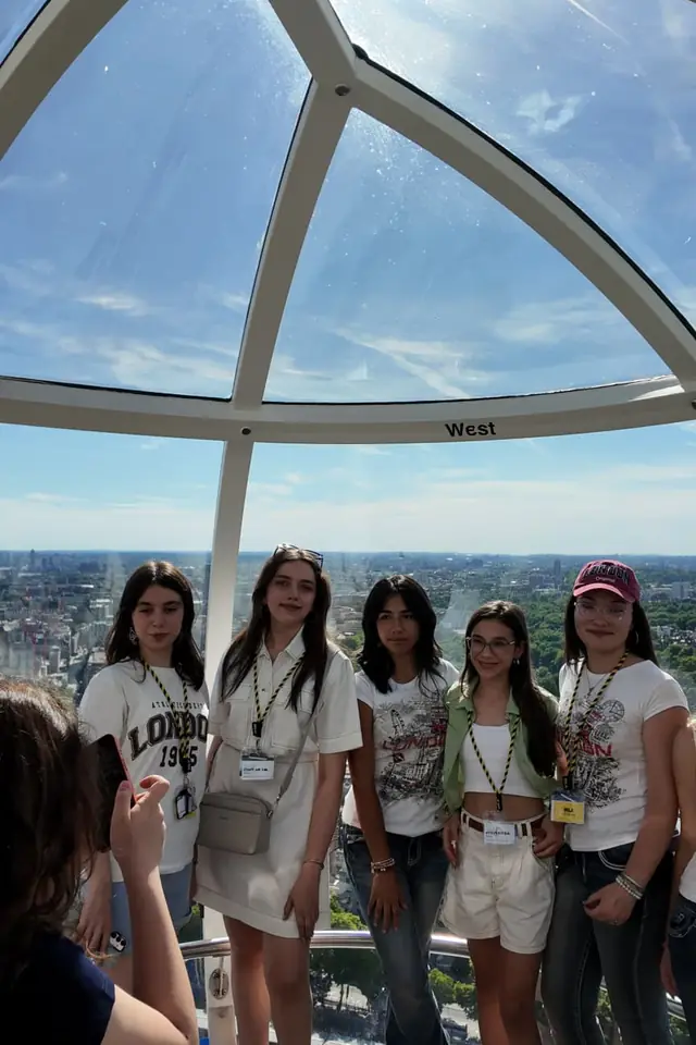 London Eye kapsülünde şehir manzarası önünde poz veren öğrenciler
